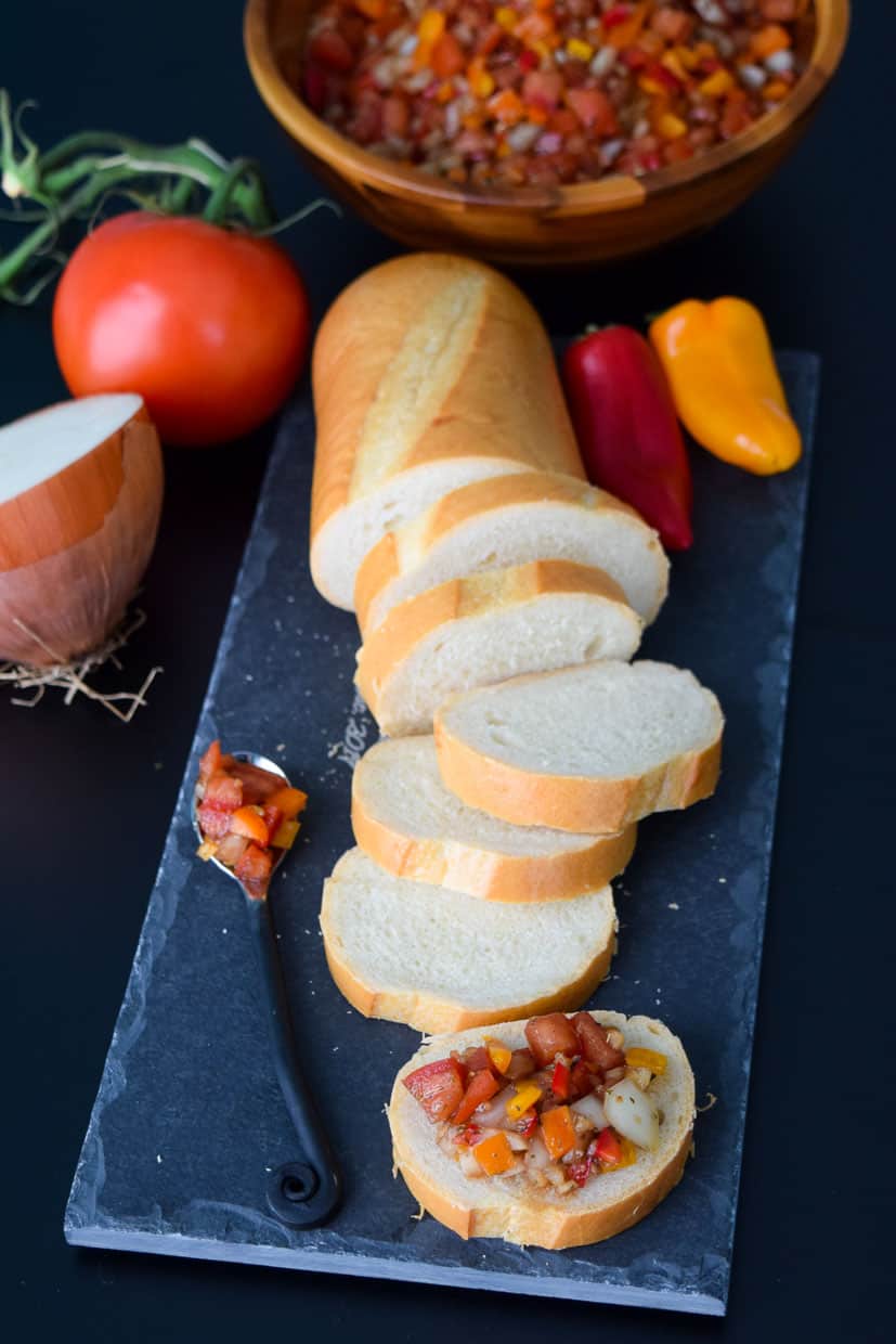 Bruschetta with Mini Peppers served on bread on slate platter with wooden bowl in background