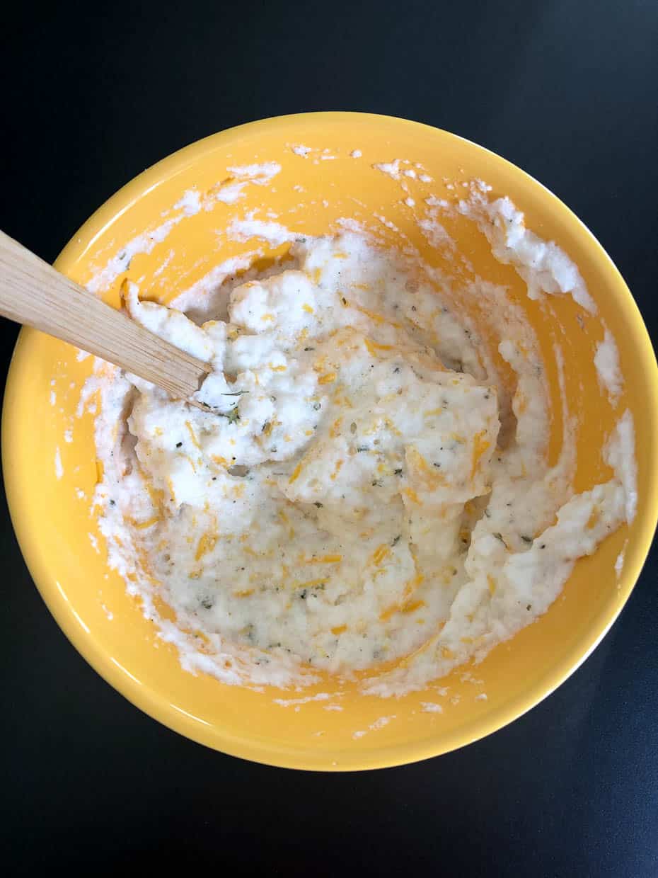 Whipped egg whites fully mixed with cheese and seasonings in yellow bowl overhead shot