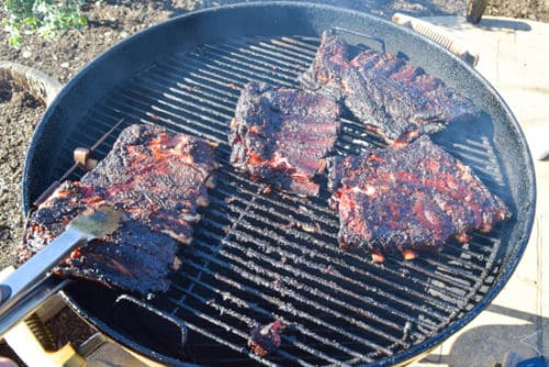 ribs being flipped on weber grill with spatula