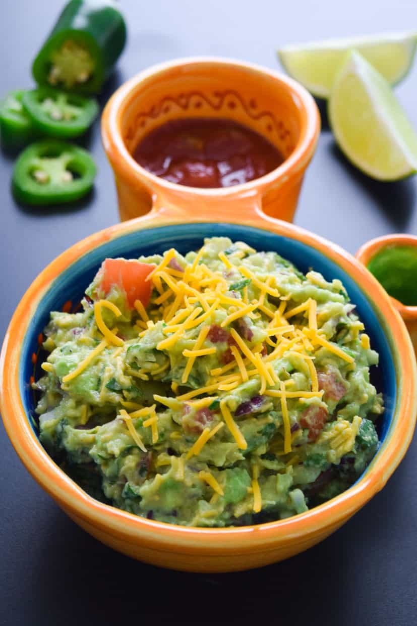 Cheesy Guacamole served in Mexican bowl with lime and jalapeños 