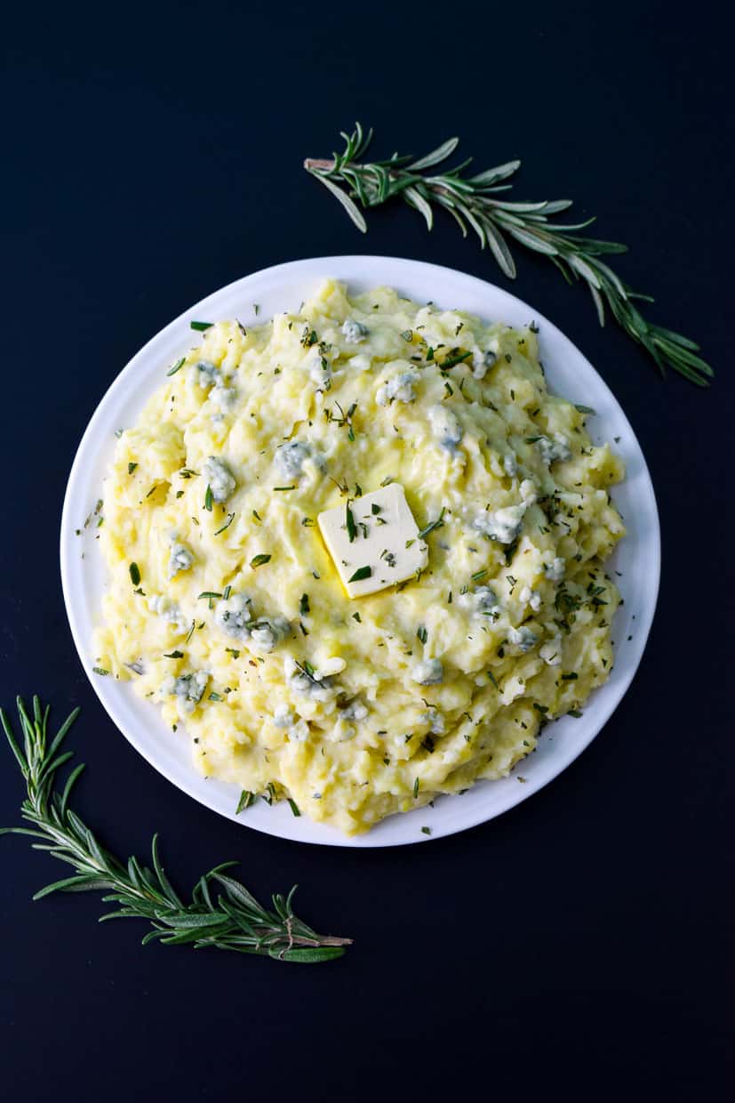 Rosemary and Blue Cheese Mashed Potatoes in white bowl with rosemary sprigs around it overhead shot