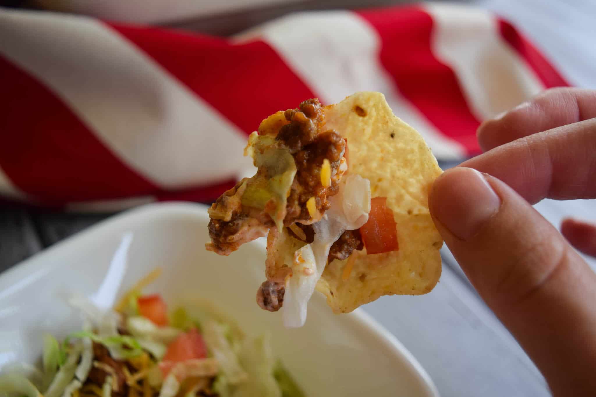 Taco dip scooped onto tortilla chip being held by hand close up view