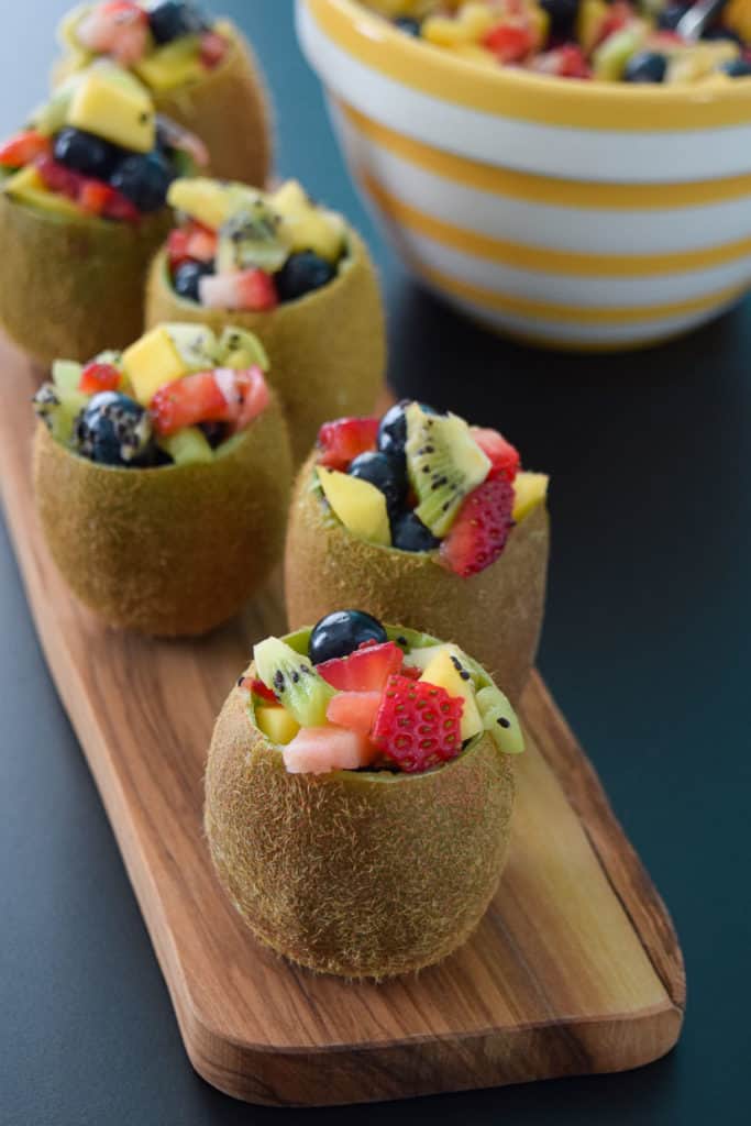Close up view of tropical fruit salad in kiwi cups on wooden platter
