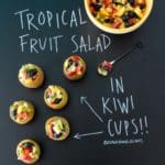 Tropical Fruit Salad in Kiwi Cups with title written on black chalkboard