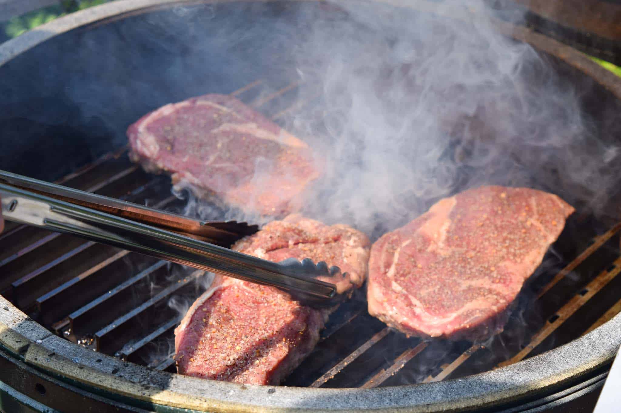 Steaks being flipped with spatula on Big Green Egg close up view