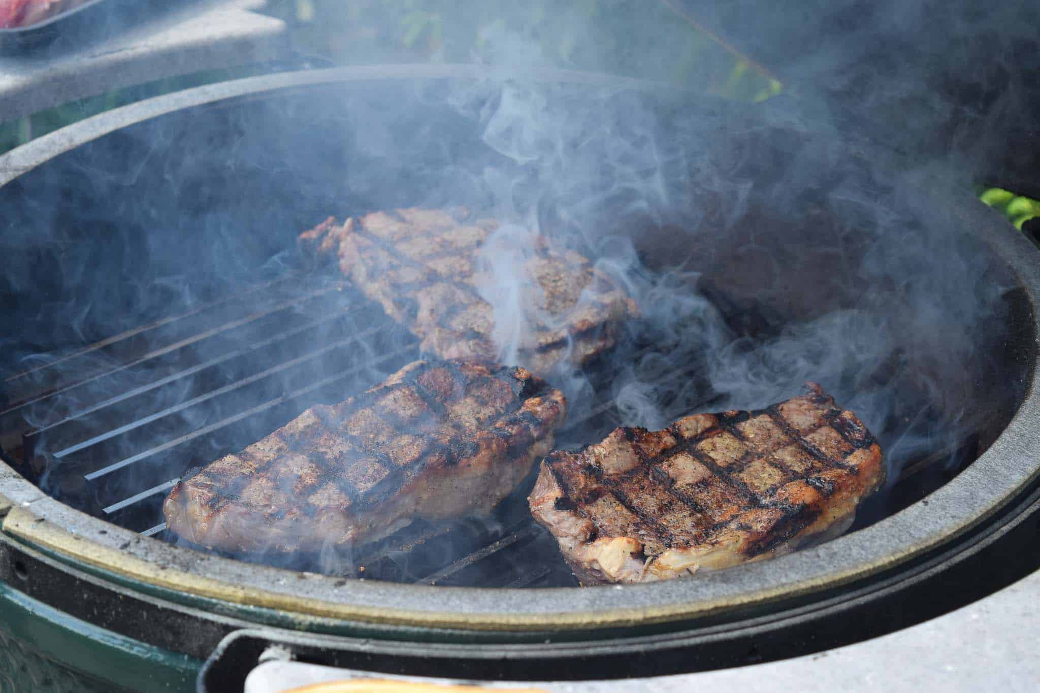Steaks being grilled on a Big Green Egg close up view with smoke rising