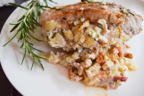 apple bacon blue cheese stuffed pork chop on white plate with sprig of rosemary close up view
