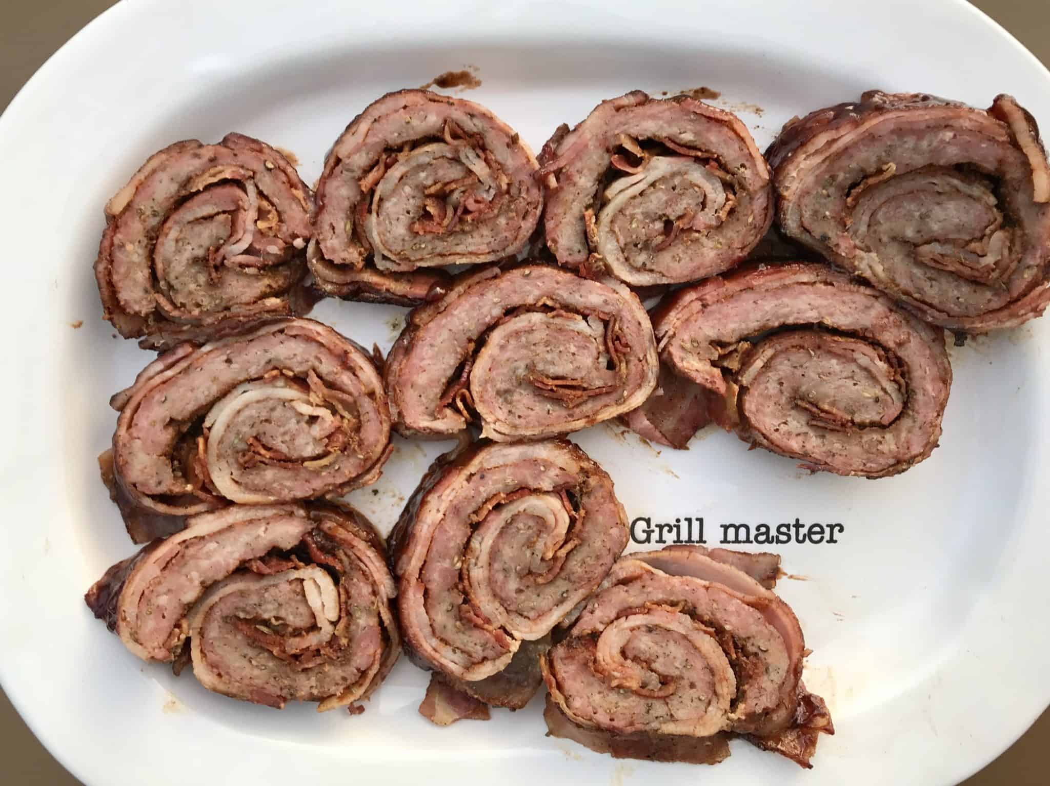 Bacon explosion cut into slices and served on white platter that says "grill master" overhead shot