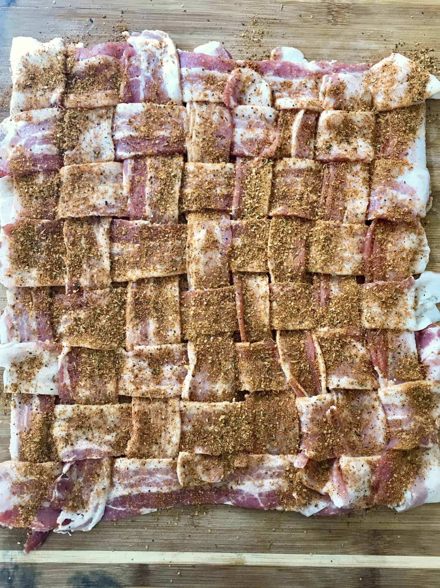 Bacon weave topped with seasonings on wooden cutting board overhead shot