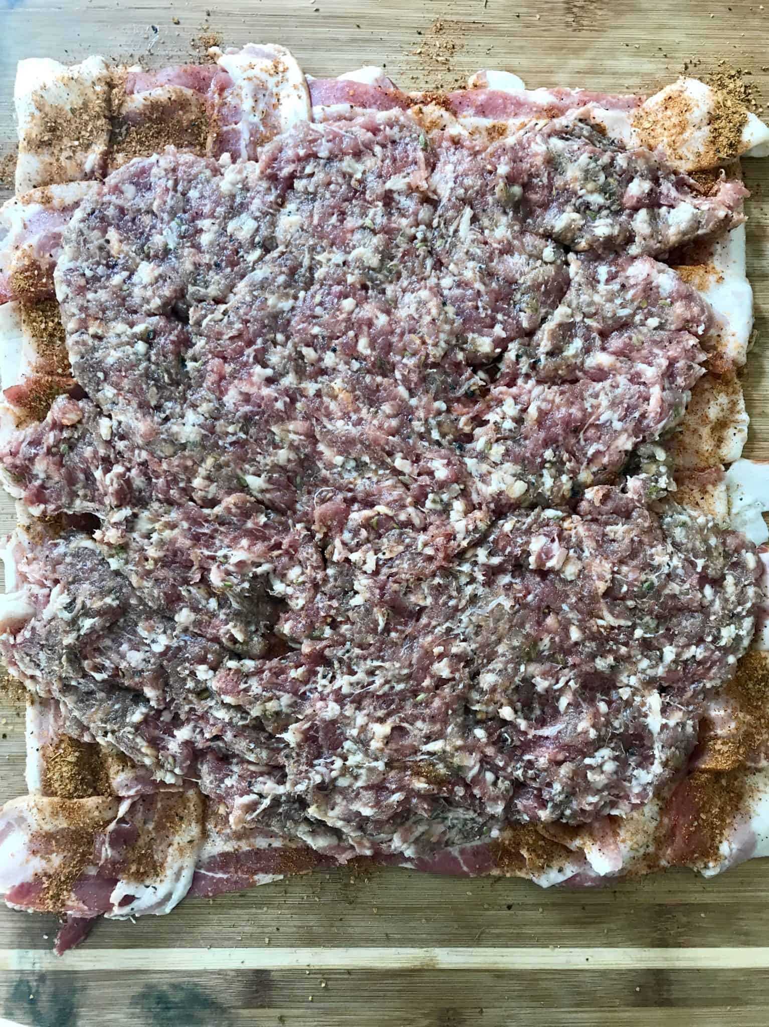 Bacon weave topped with ground sausage on wooden cutting board overhead shot