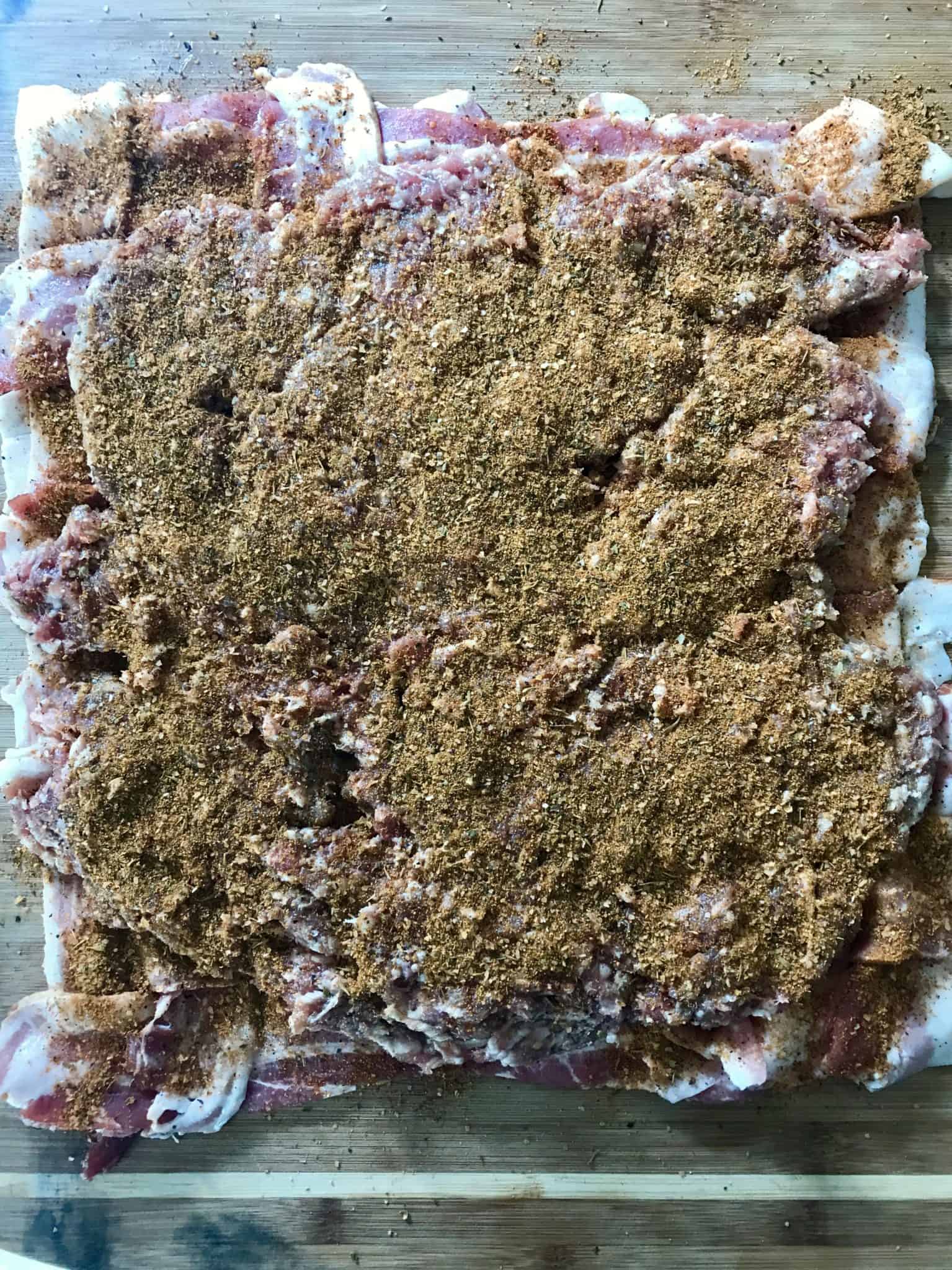 Bacon weave topped with ground sausage and seasonings on wooden cutting board overhead shot