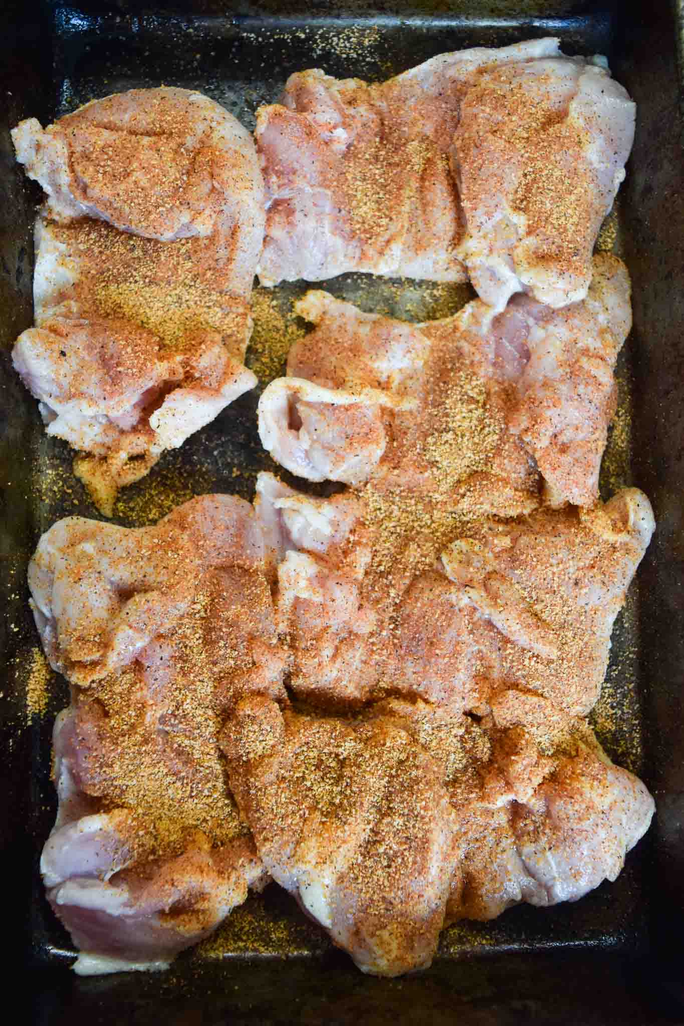 Chicken thighs on baking sheet covered in seasonings overhead shot