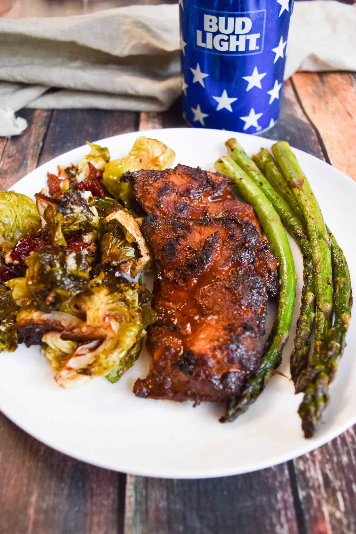BBQ chicken thighs on plate with asparagus and bud light can in background