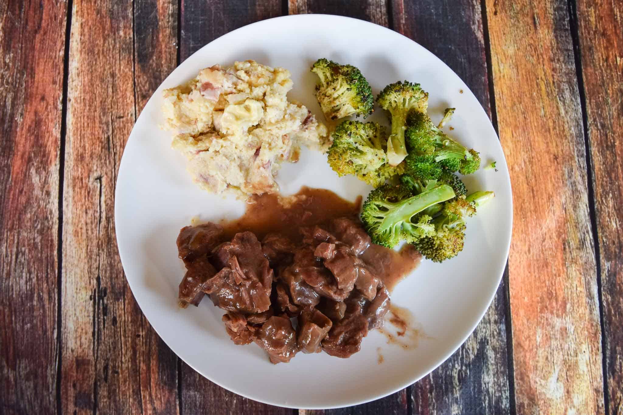 Crock Pot steak on white plate with broccoli and mashed cauliflower overhead shot