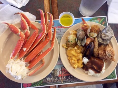 Plate of crab legs beside plate of various side dishes overhead shot 