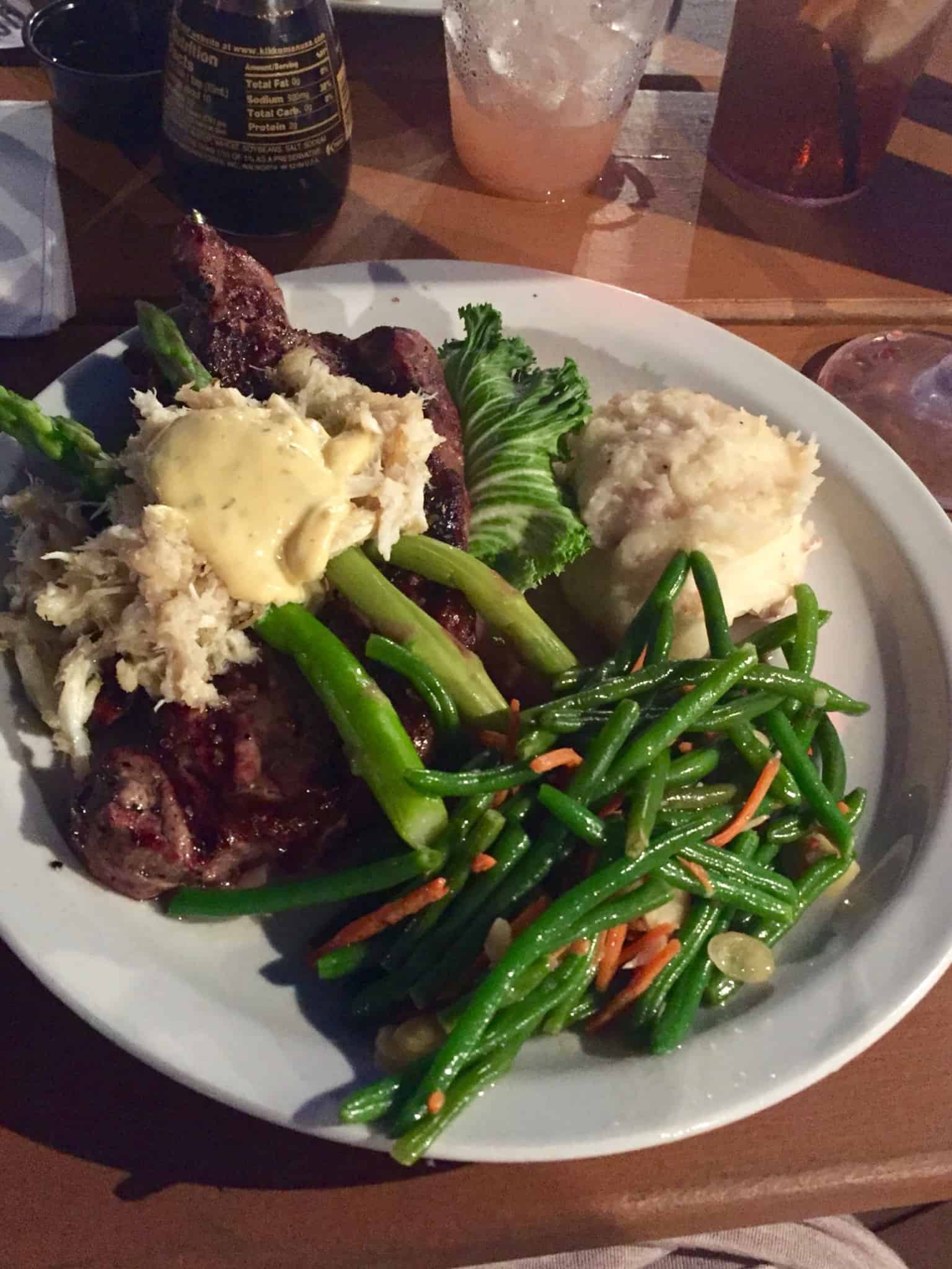 White plate with steak topped with crab served with vegetables and mashed potatoes 