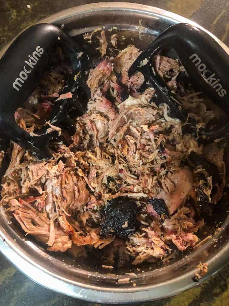 Pork butt being shredded in bowl with shredding claws overhead shot