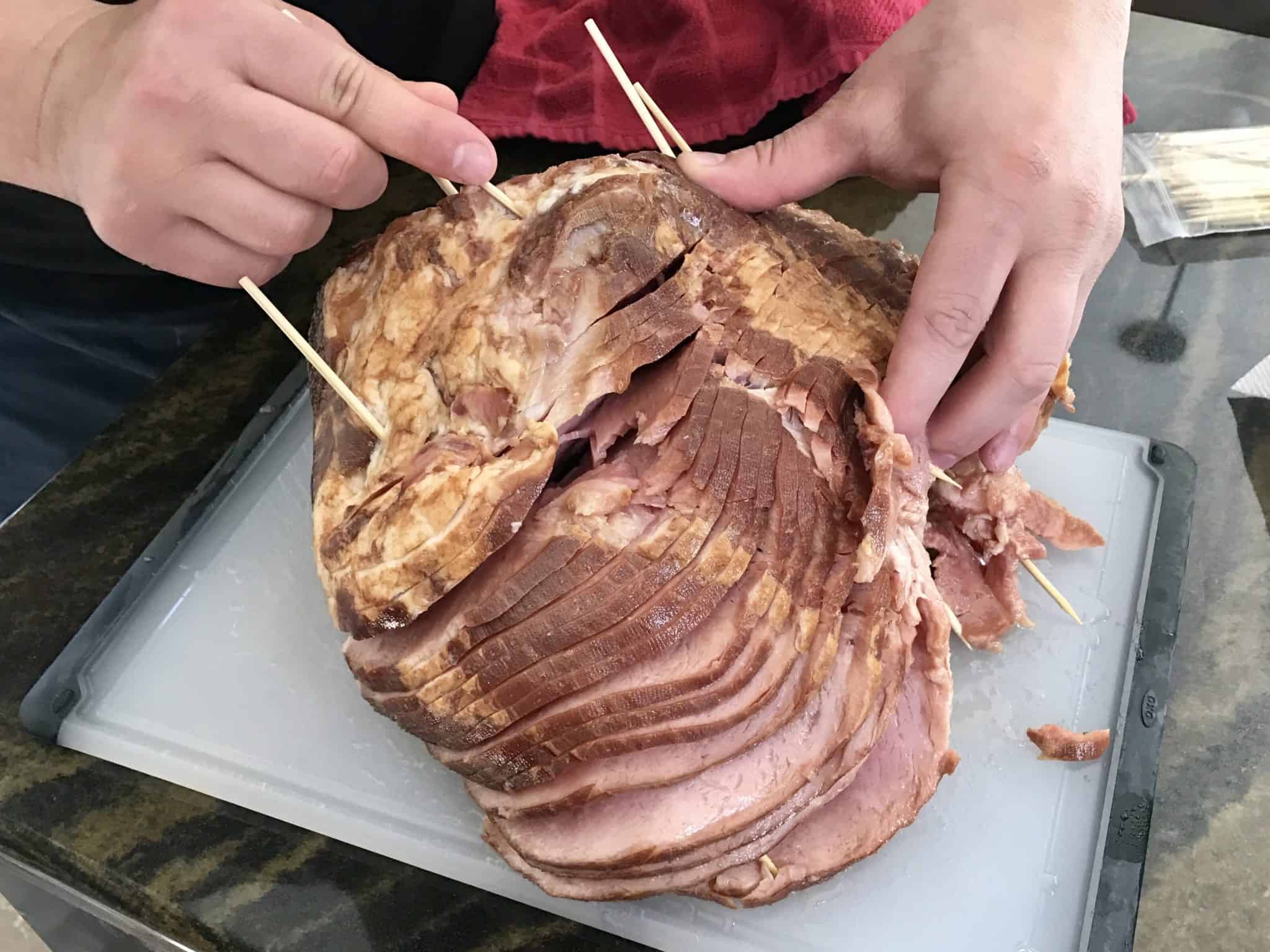 Sliced ham being held together with skewers on white cutting board