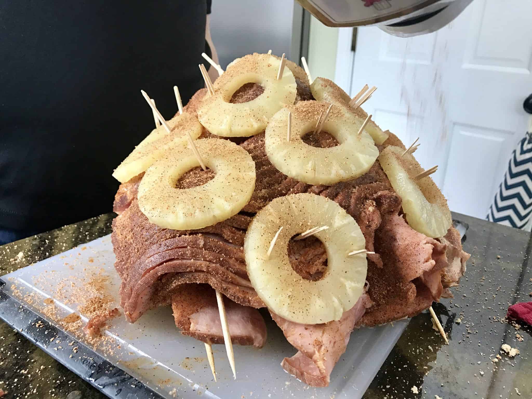 Sliced ham with pineapples on skewers all over it 