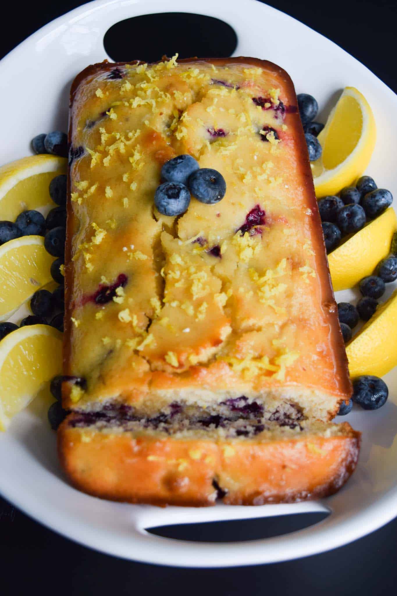 lemon blueberry bread in white platter surrounded by lemon slices and blueberries up close view
