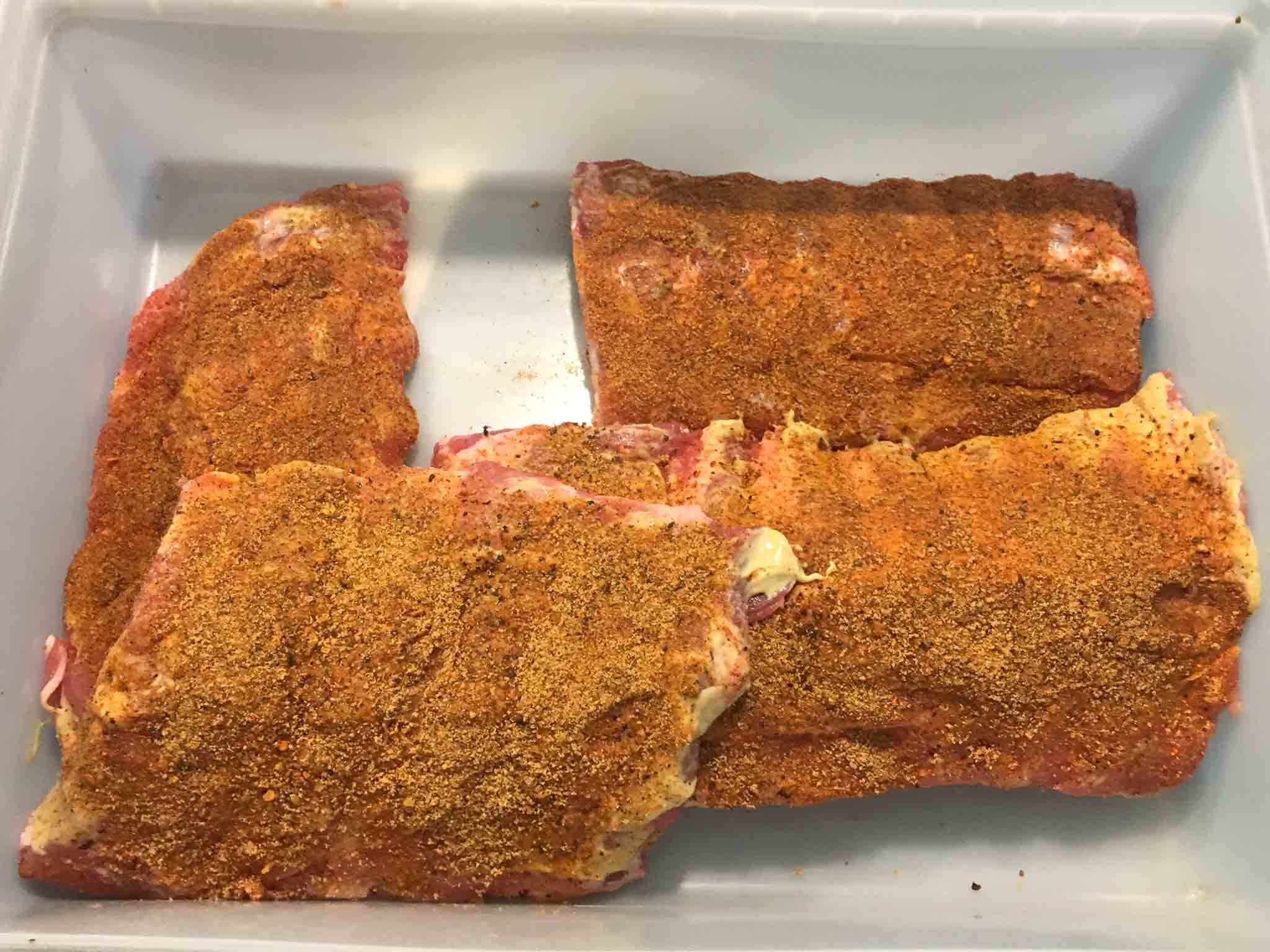 racks of ribs covered in dry rub in white container overhead shot