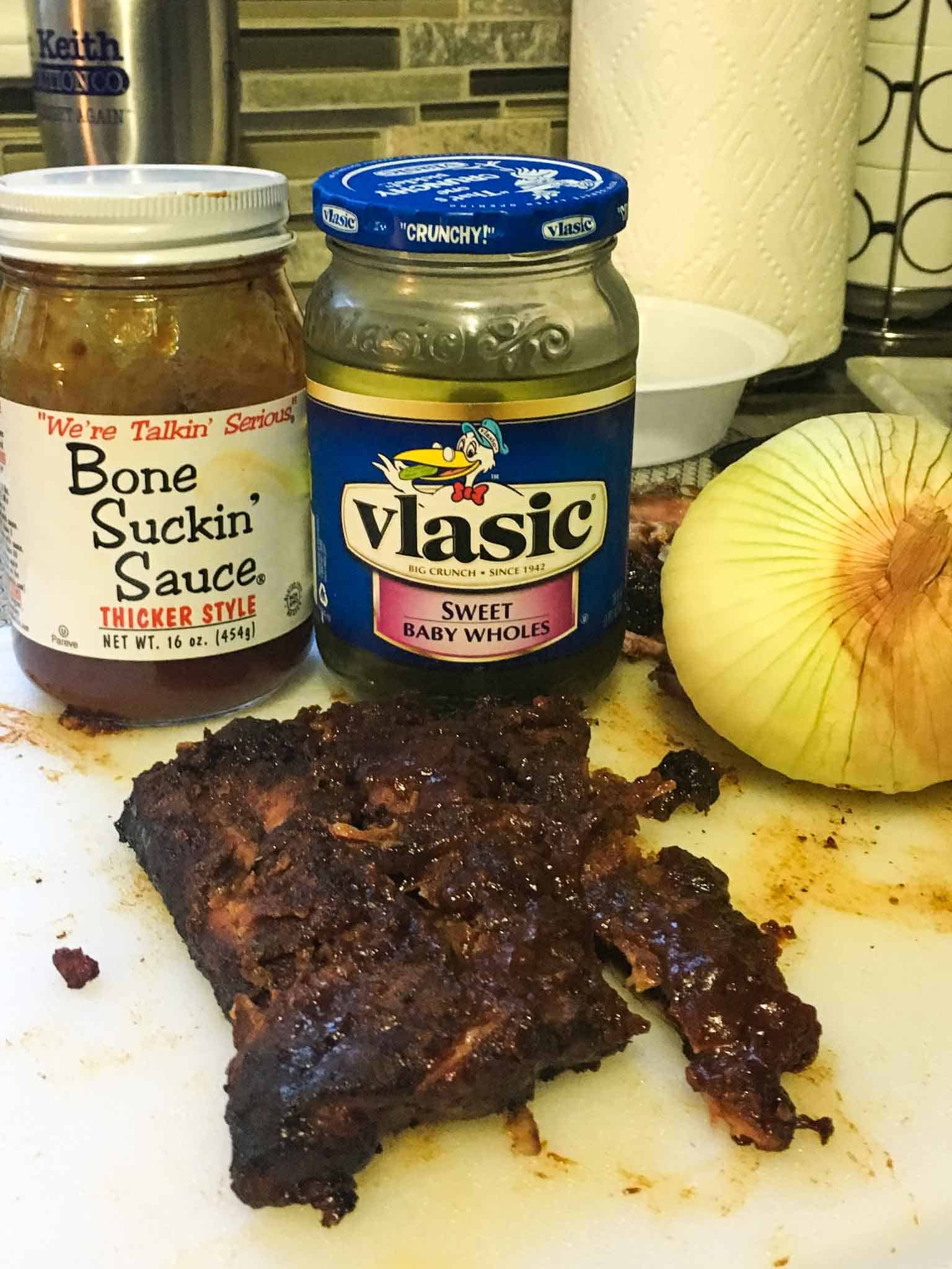 ribs sitting in front of BBQ sauce pickles and onion close up view