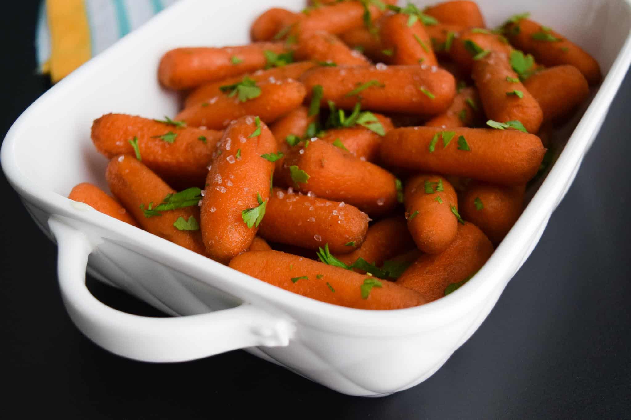 Honey Balsamic Roasted Carrots topped with parsley and salt in white serving dish close up