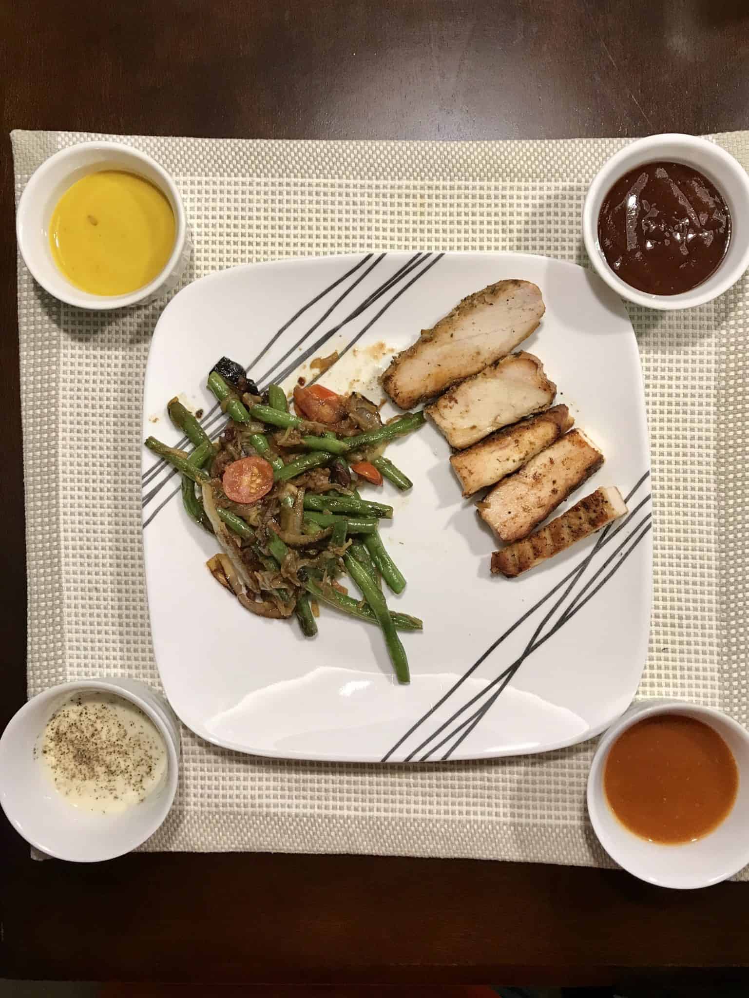 Chicken breast served on white plate with vegetables and 4 different sauces