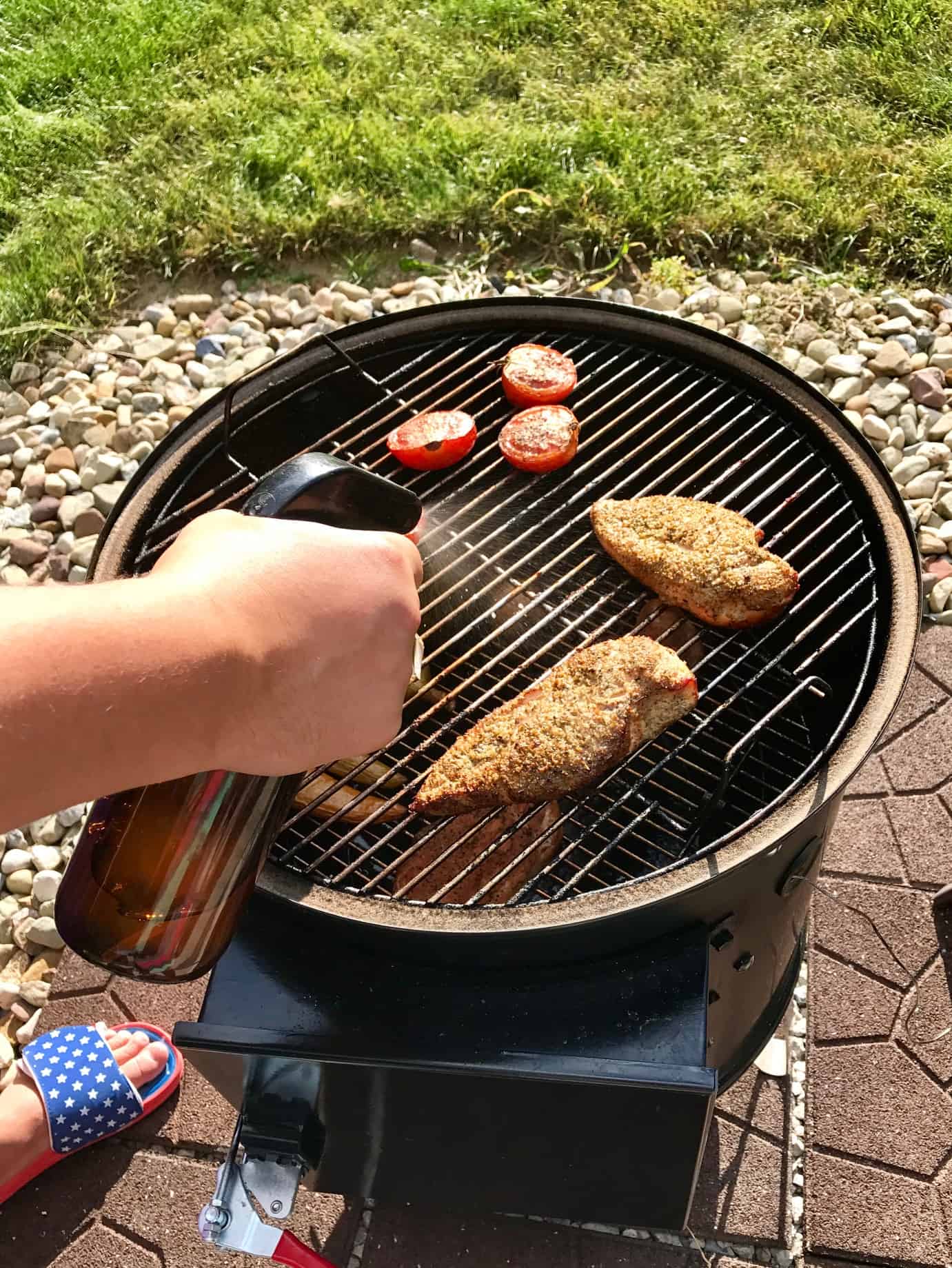 Spritzing chicken breasts on weber grill with water bottle 