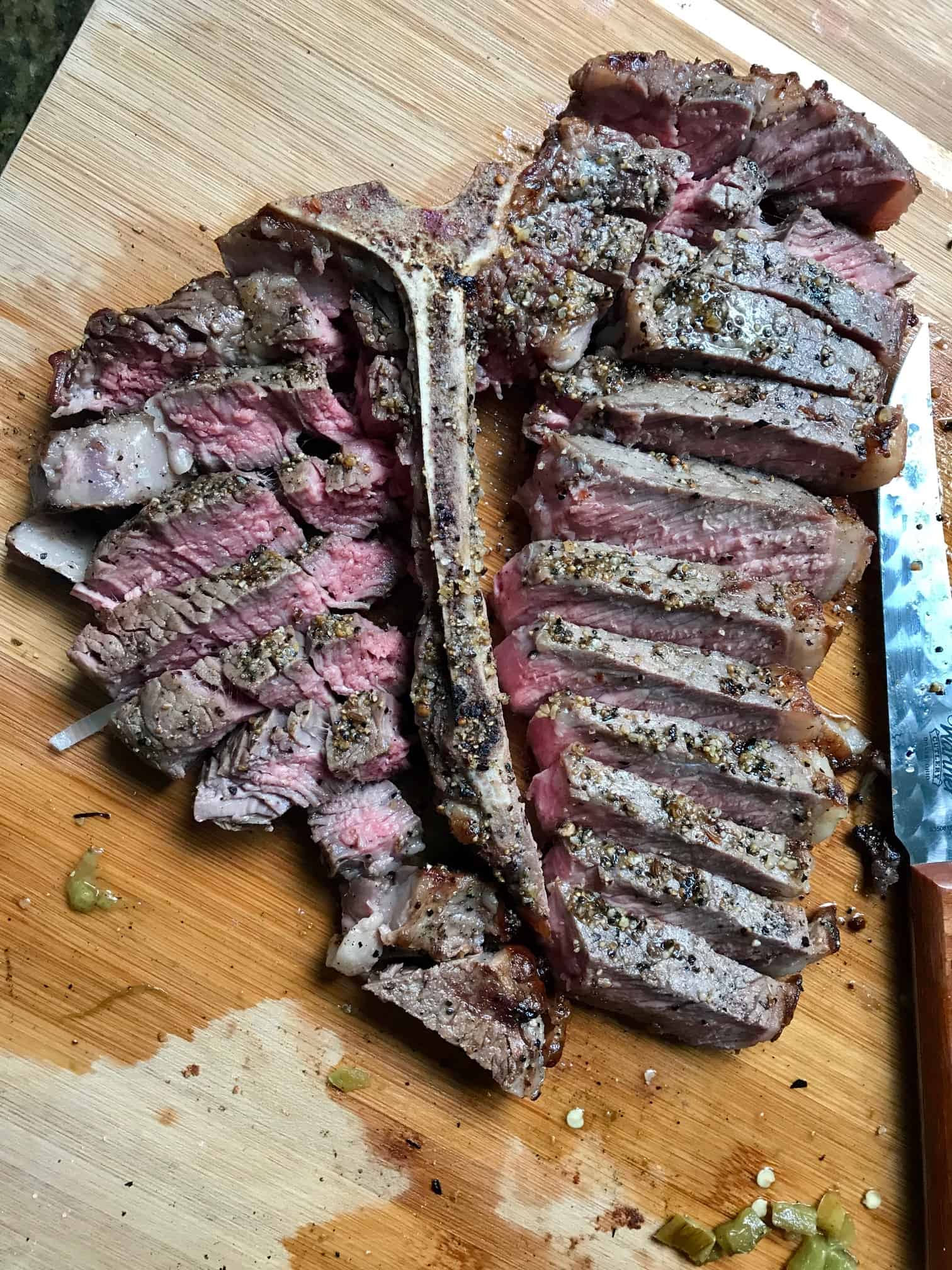 Reverse Sear Steak slices by bone on wooden cutting board