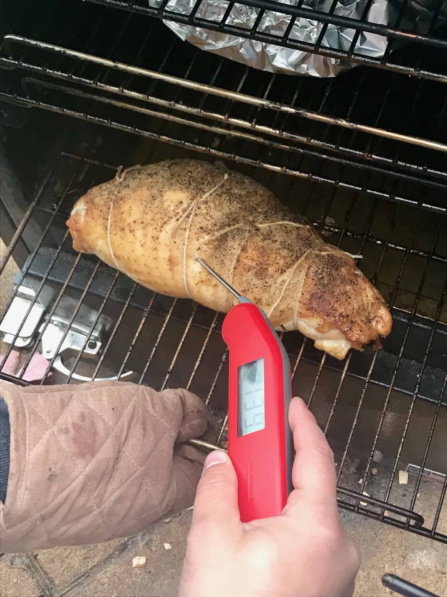 Turkey Porchetta in smoker being checked with meat thermometer side view