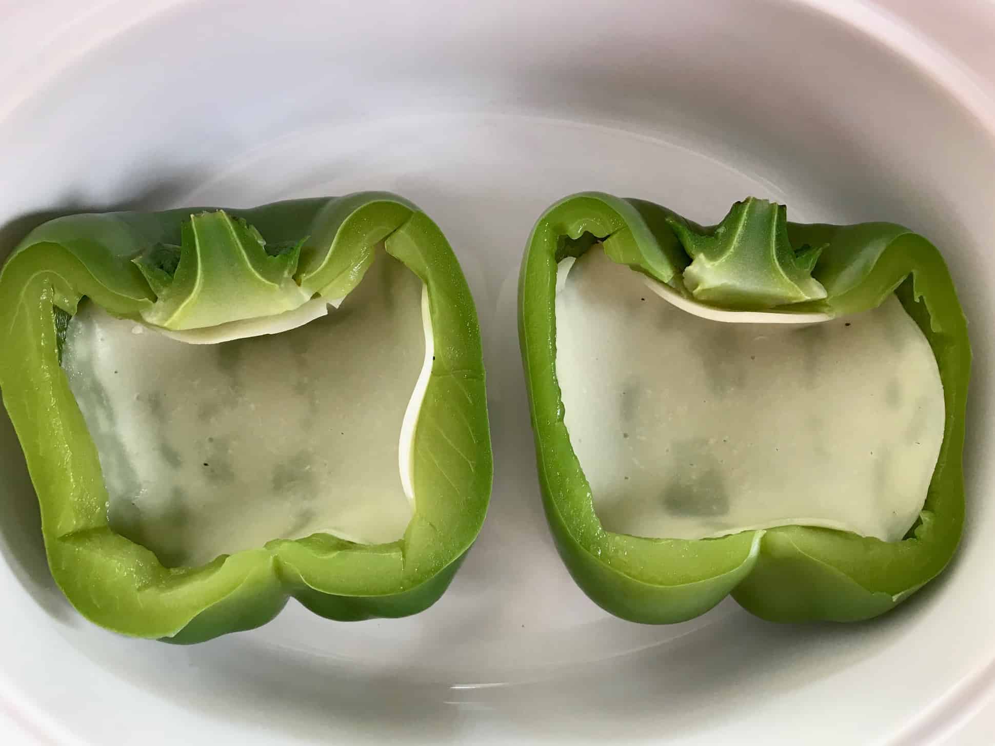 Green pepper sliced in half with provolone cheese inside in white bowl overhead shot