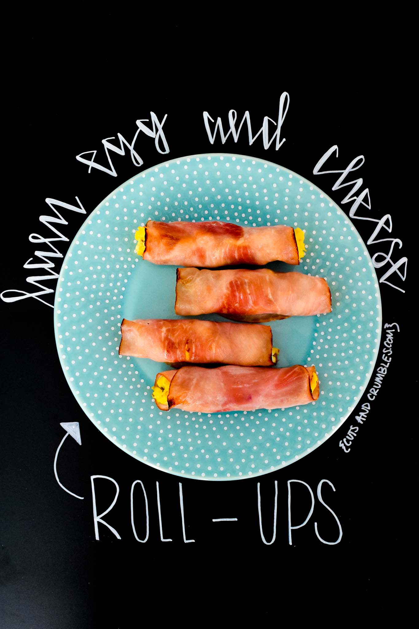 Ham Egg and Cheese Roll-Ups on blue plate with title written on chalkboard