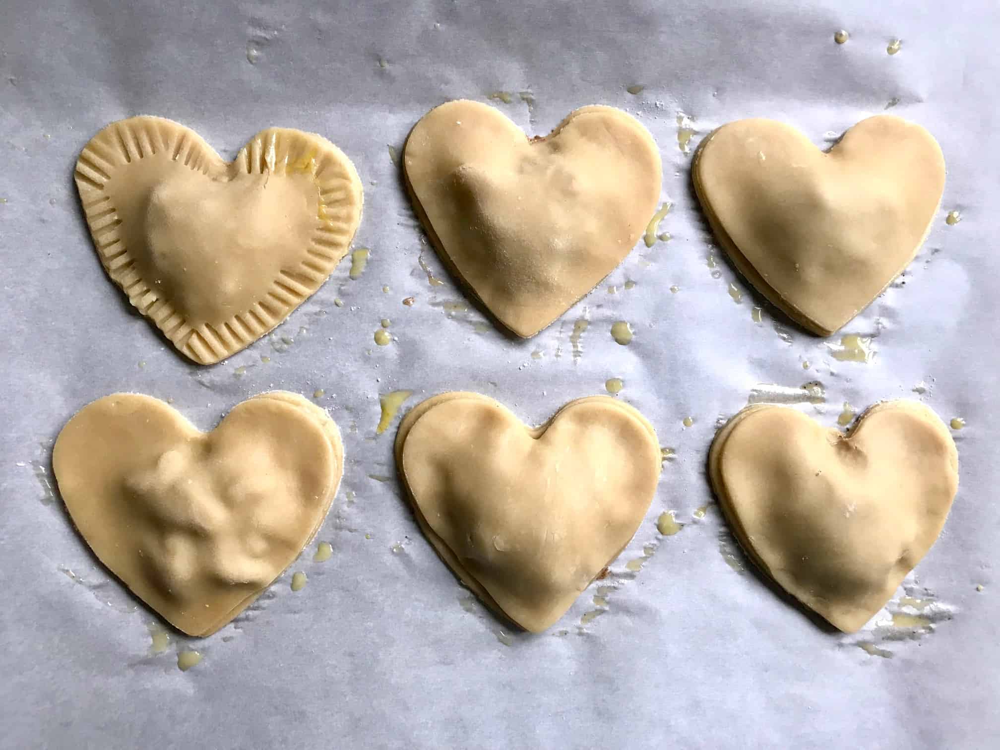 Apple Pie heart shaped pastries on baking sheet pressing edges down with fork overhead shot