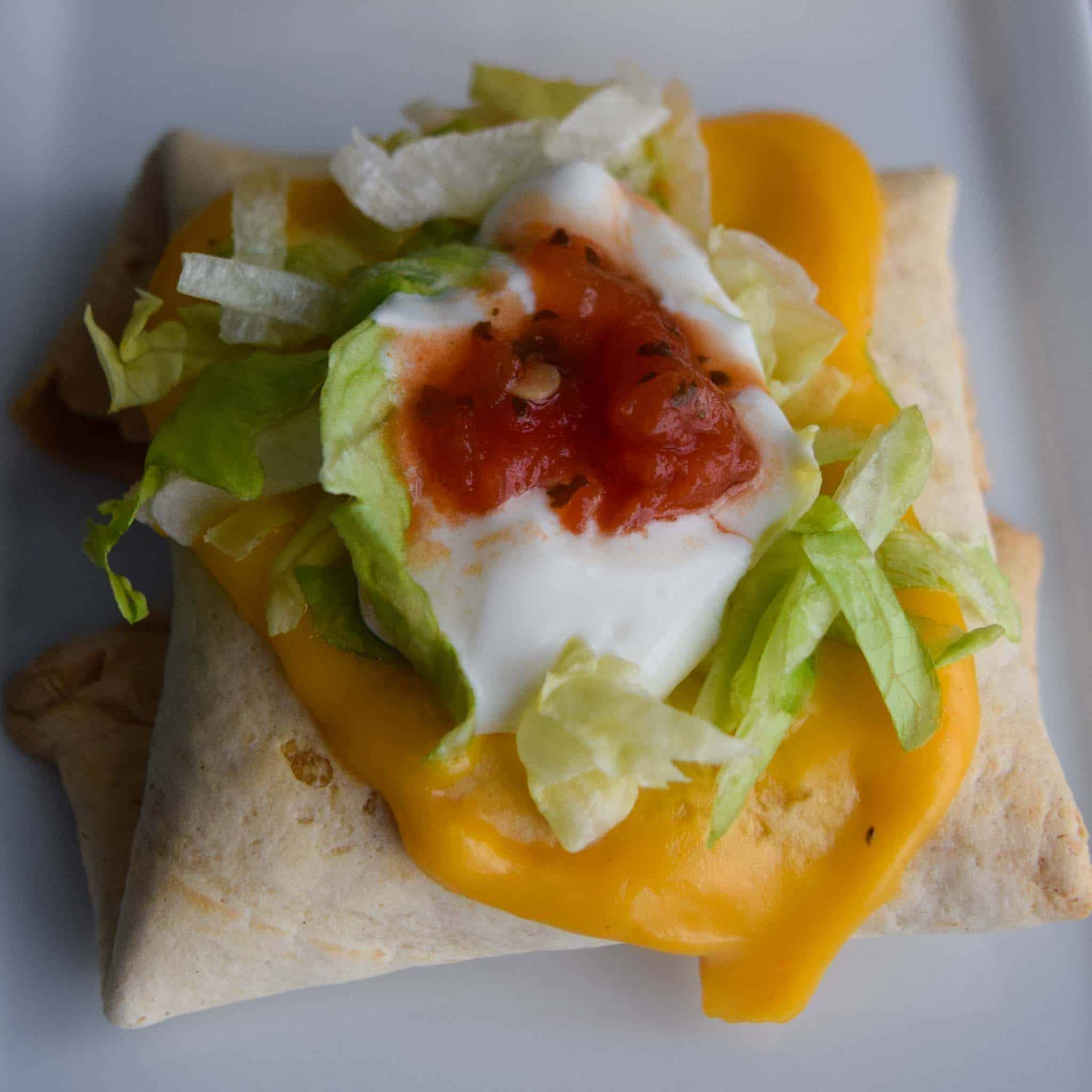 Baked Chimichangas with Guilt-Free Cheesy Sauce topped with lettuce sour cream and salsa close up view