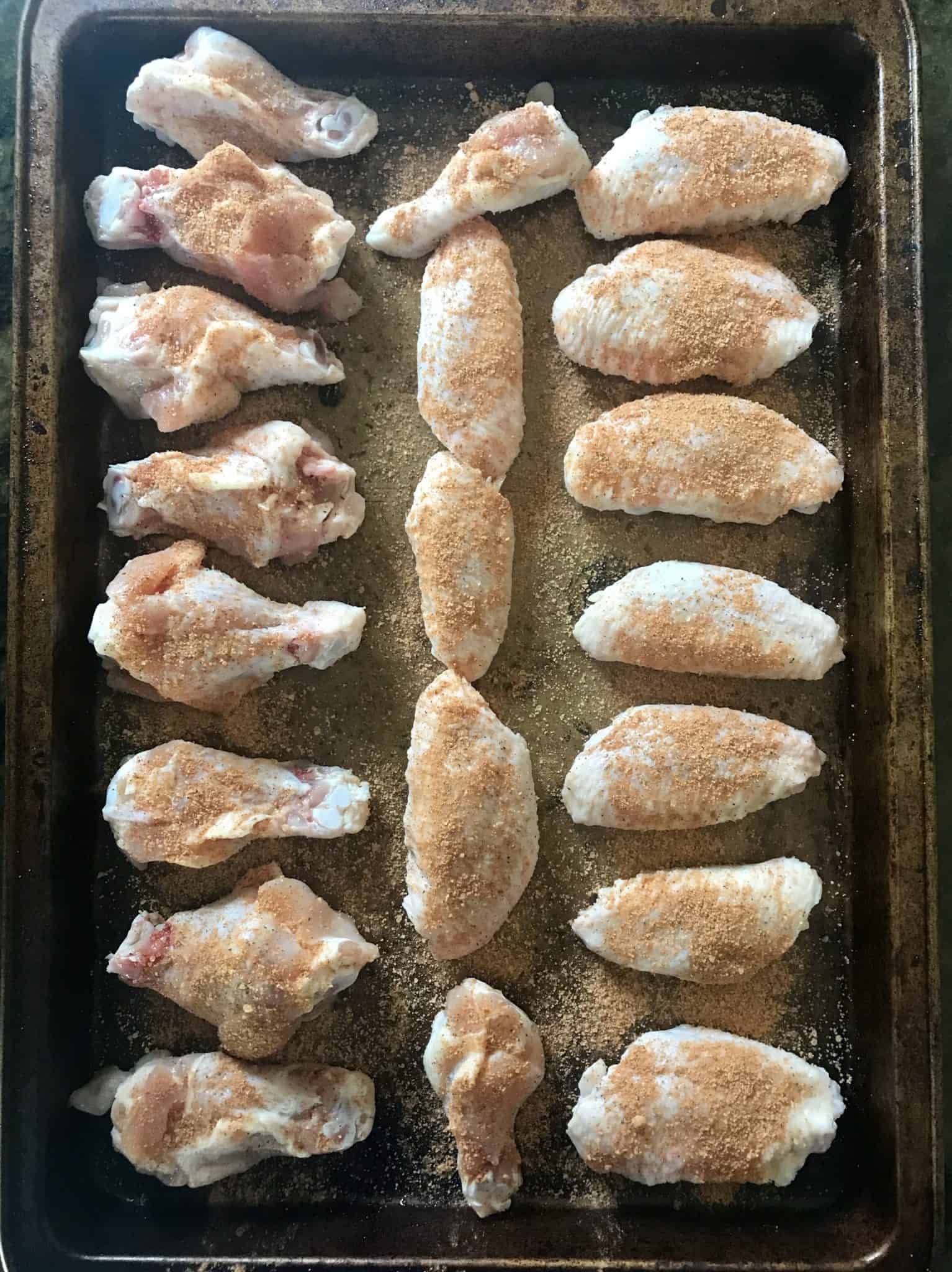 Seasoned chicken wings ready to be cooked lined up on baking sheet overhead shot