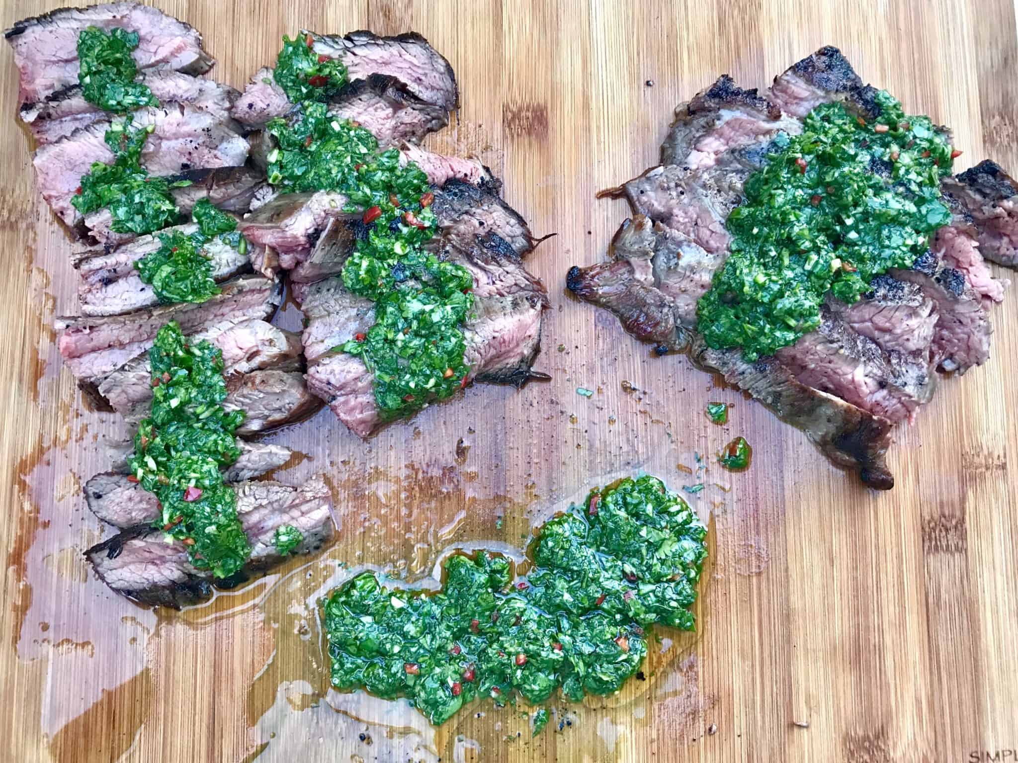 Chimichurri Sauce on top of multiple slices of steak on wooden cutting board overhead shot