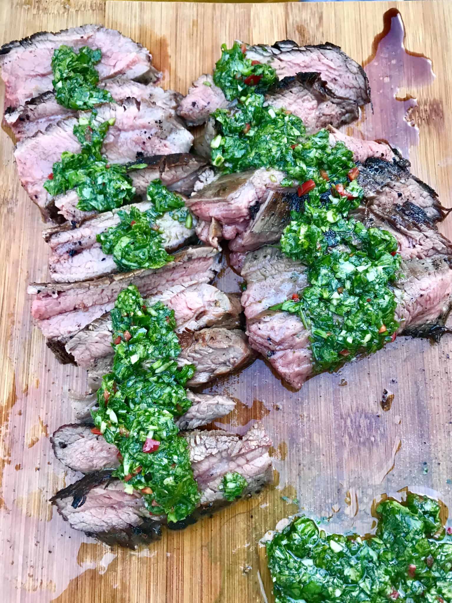 Caveman Style Flank Steak sliced on wooden cutting board topped with chimichurri sauce overhead shot