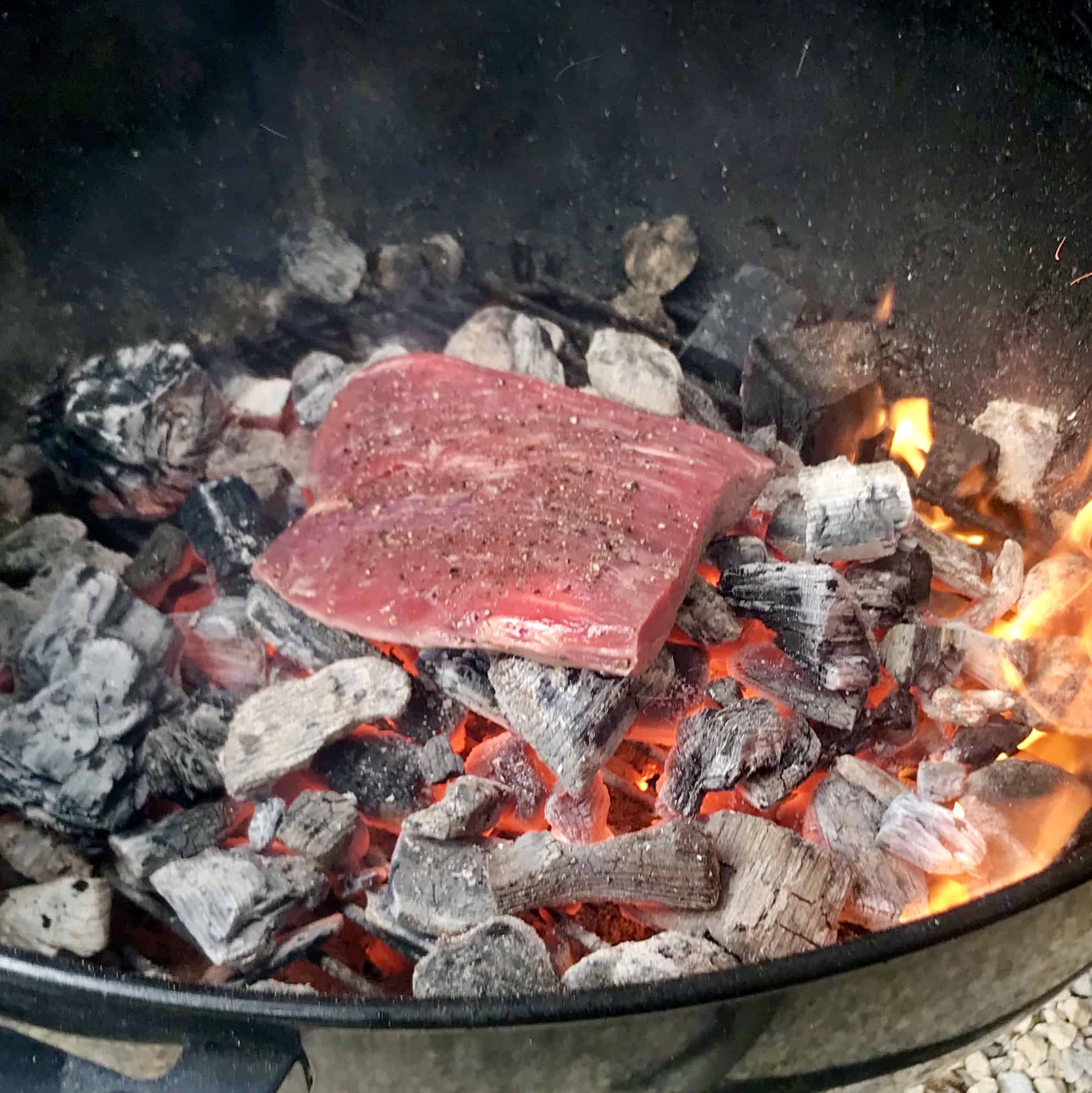 Raw steak being cooked directly on hot coals close up view