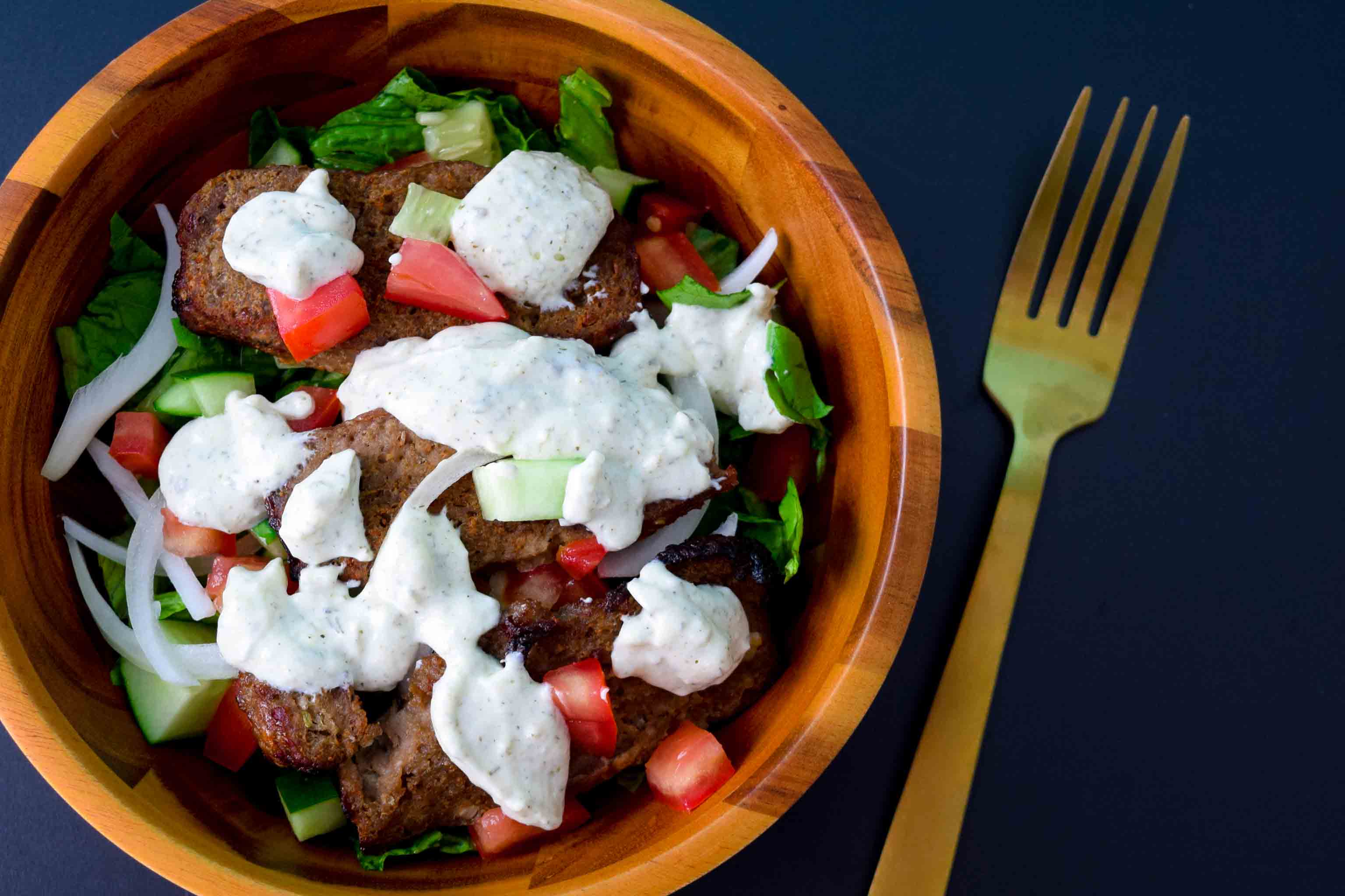 Gyro meat in salad bowl covered in tzatziki sauce on black background