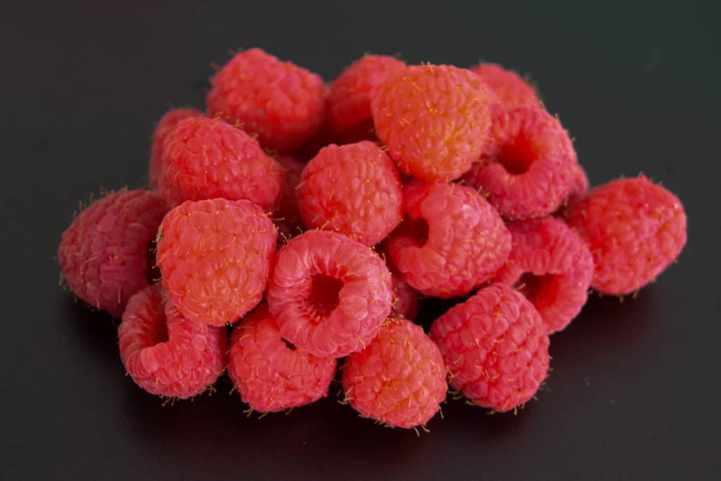 a pile of raspberries on black background