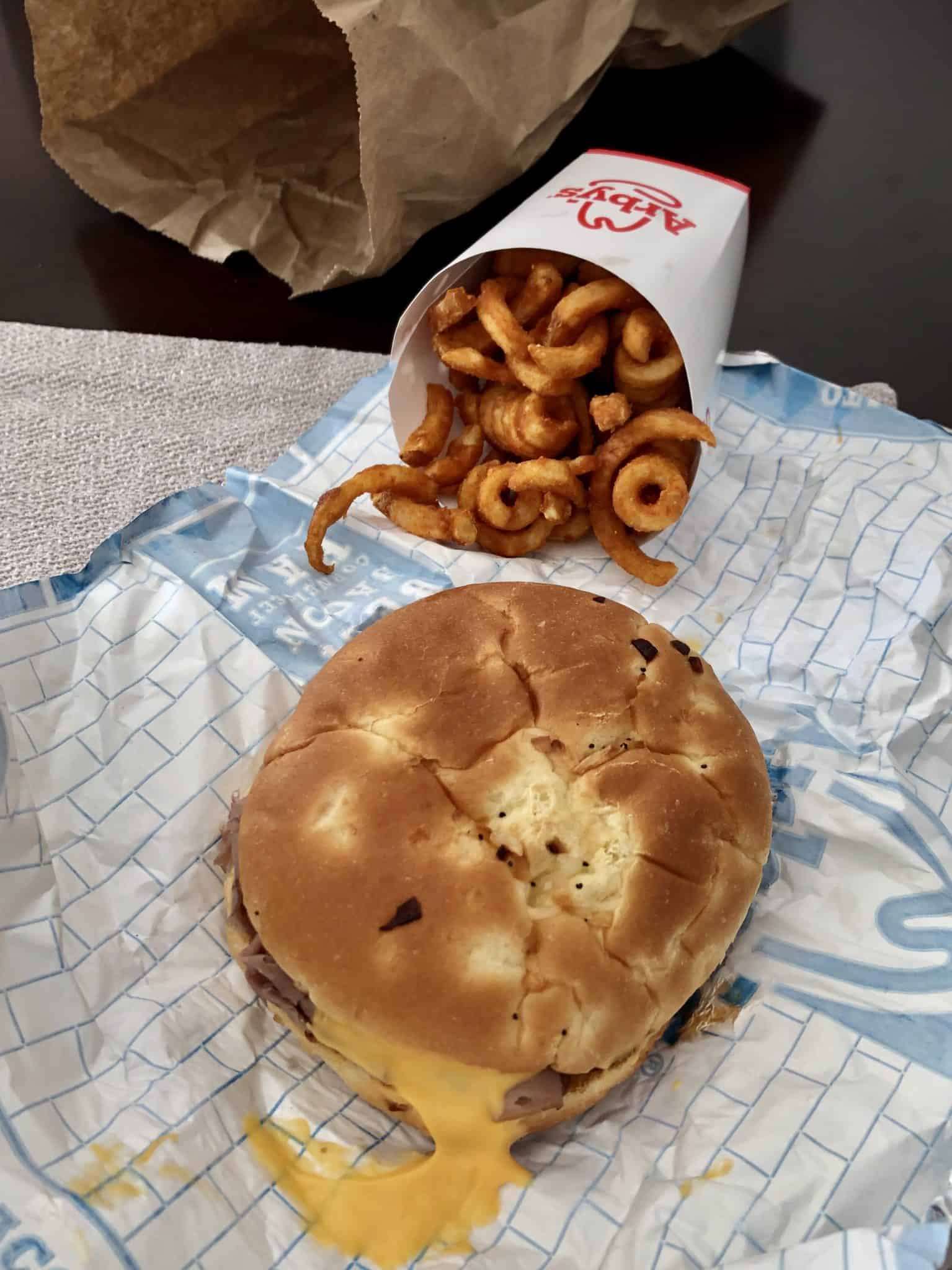 Arby's beef and cheddar with curly fries in background