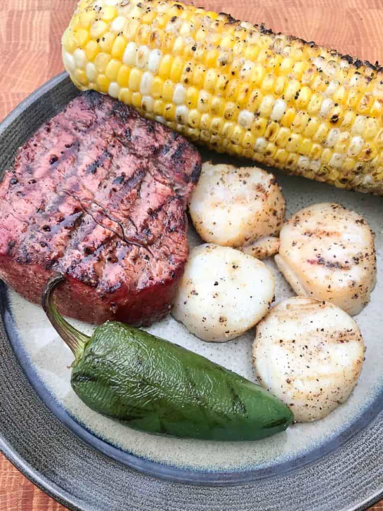 Smoked scallop served on plate with steak jalapeño and corn on the cob
