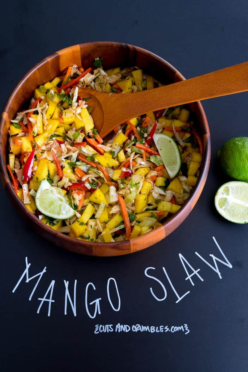 Mango slaw in wooden bowl with title written on chalkboard