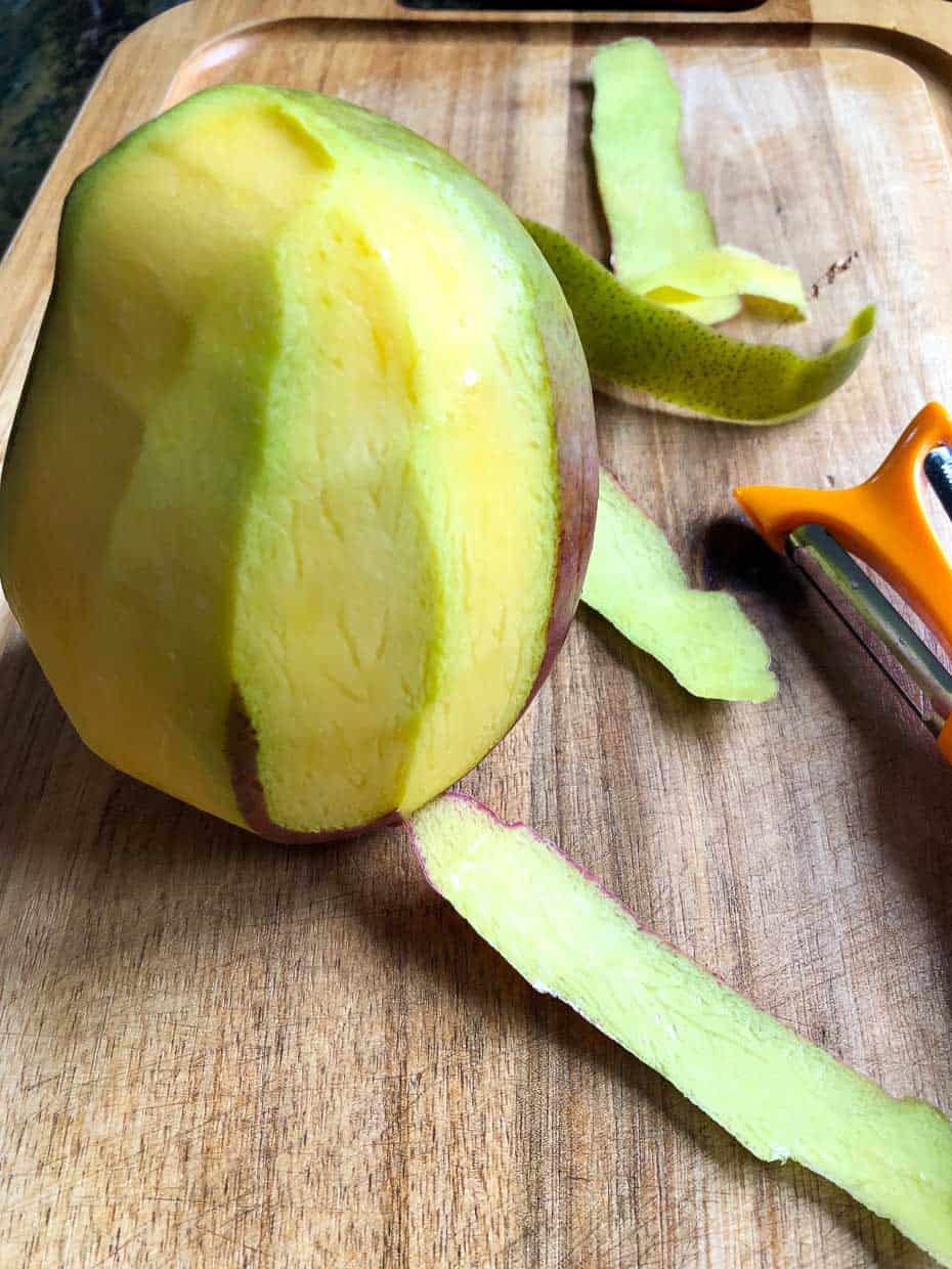 Mango sitting on cutting board having skin peeled off