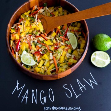 Mango slaw in wooden bowl with title written on chalkboard
