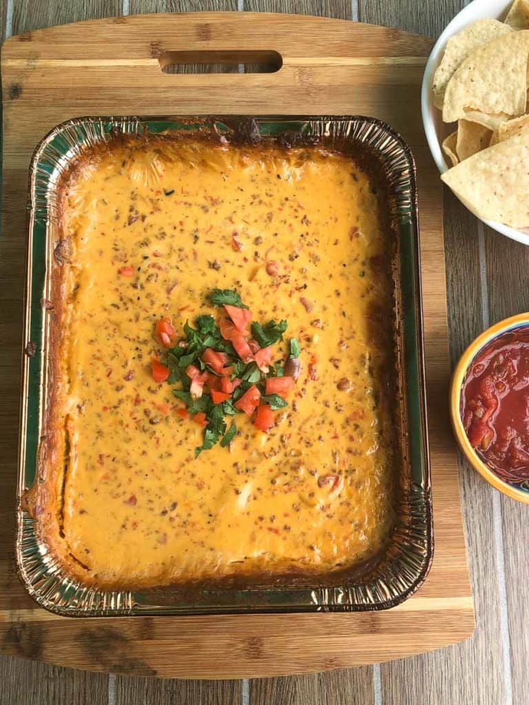 smoked queso dip topped with cilantro and diced tomato next to bowl of salsa with chips