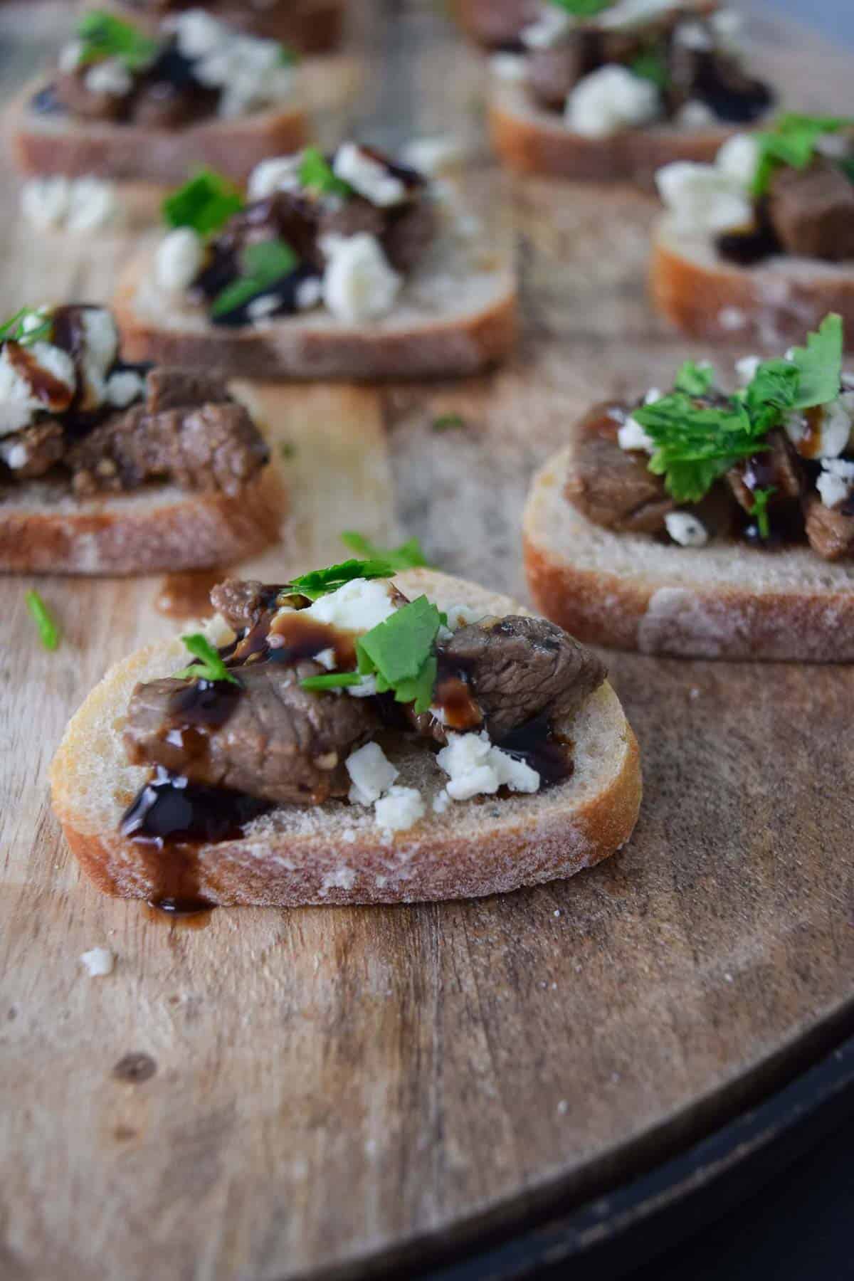 Blue Cheese and Steak Crostini on wooden platter close up view