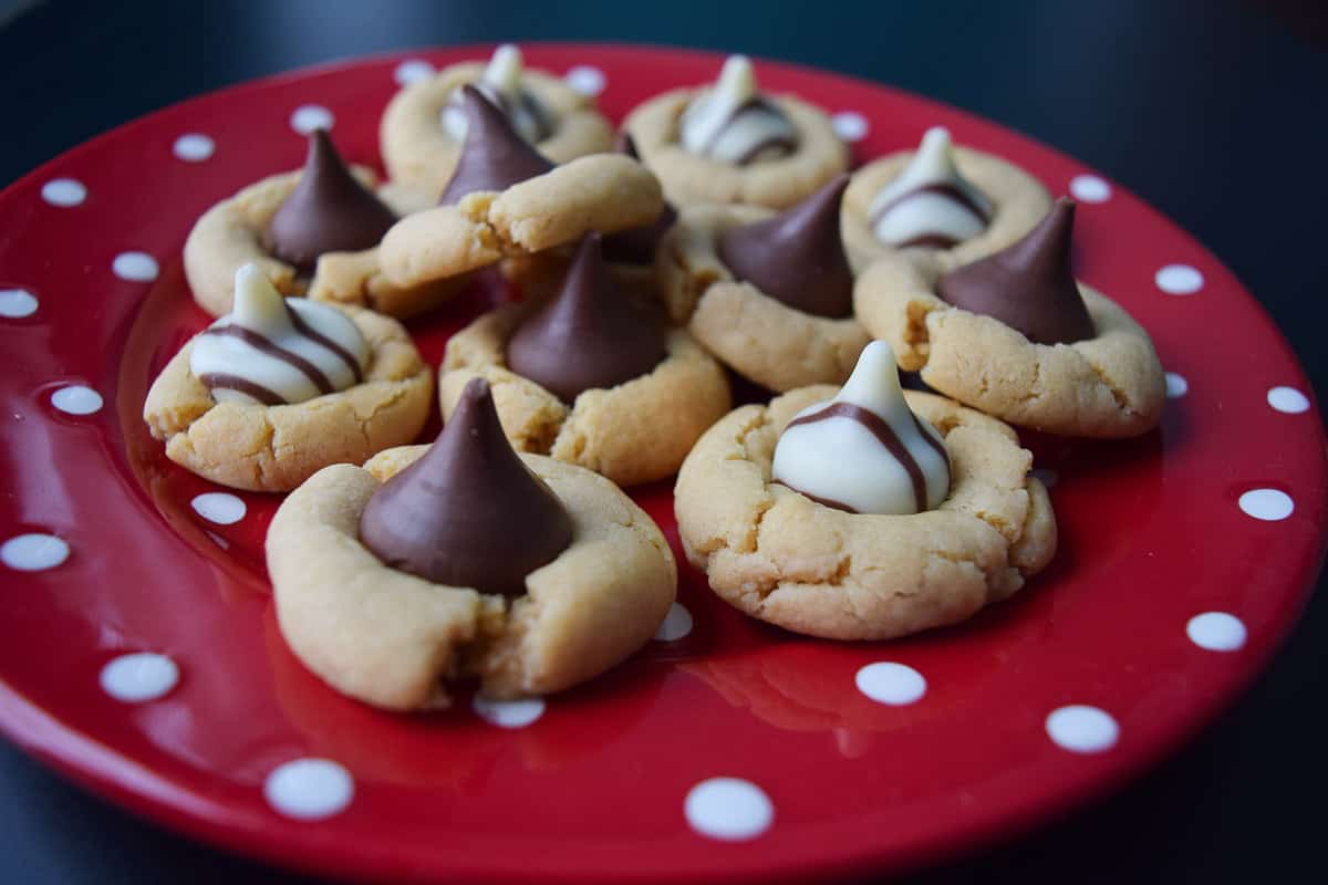 peanut butter cookies topped with Hershey kisses and hugs on red and white polka dot plate close up view
