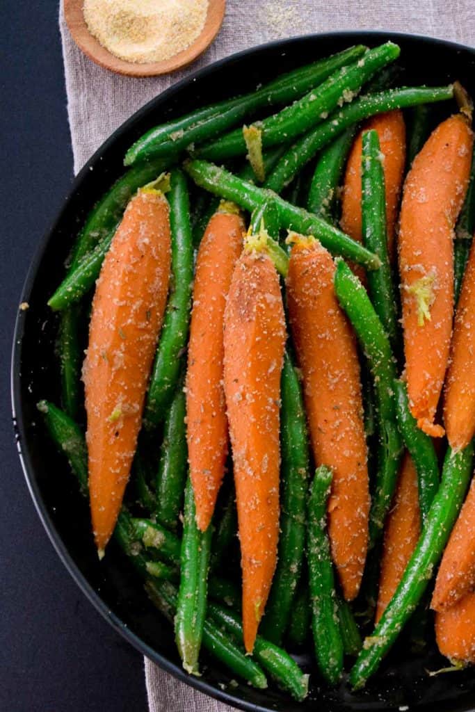 overhead close up shot of black bowl with carrots and green beans 
